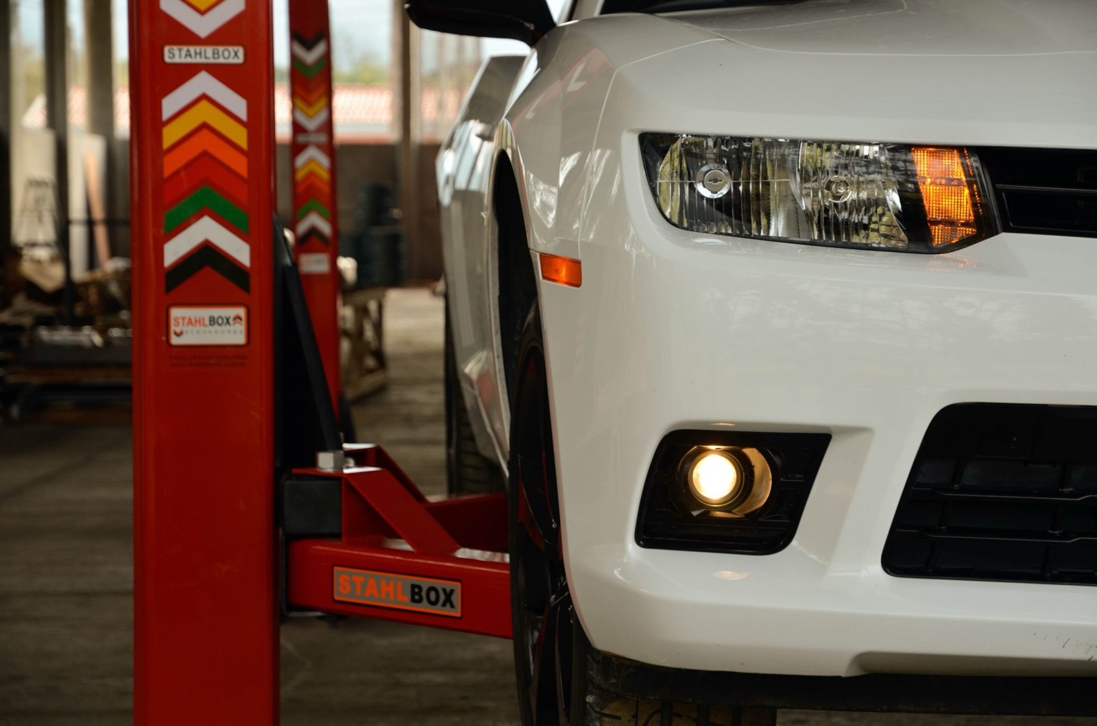 Duas colunas de elevador Stahlbox ao lado da frente de um Chevrolet Camaro branco em uma oficina